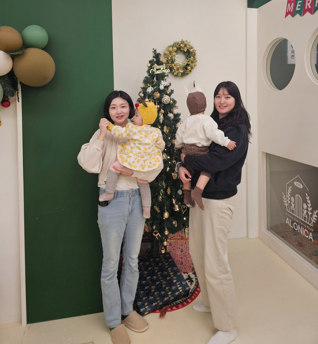 Юн Сан Хи (слева) и Ли Сон Хи  позируют для фотографии, держа своих малышей перед рождественской елкой в  ​​детском кафе. (Чхве Чжэ Хи / The Korea Herald)