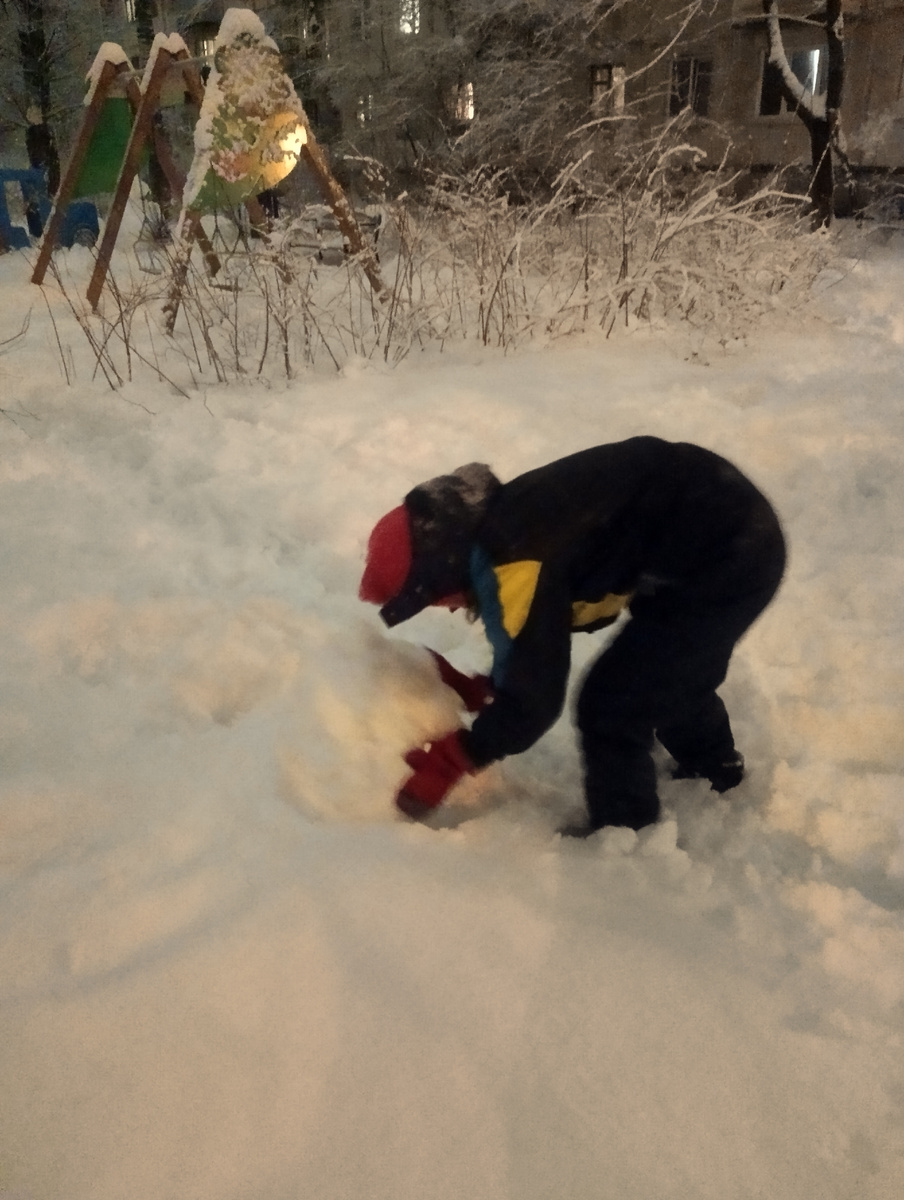 Незрячий ребёнок учиться катать ком снега. 