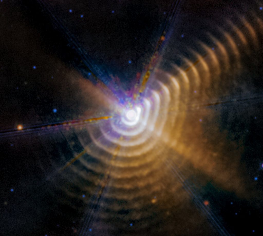    Astronomers using the NASA/ESA/CSA James Webb Space Telescope James Webb Space Telescope have identified two stars responsible for generating carbon-rich dust a mere 5000 light-years away in our own Milky Way galaxy. As the massive stars in Wolf-Rayet 140 swing past one another on their elongated orbits, their winds collide and produce the carbon-rich dust. For a few months every eight years, the stars form a new shell of dust that expands outward — and may eventually go on to become part of stars that form elsewhere in our galaxy. Every shell is racing away from the stars at more than 2600 kilometers per second, almost 1% the speed of light. Wolf-Rayet 140 lies just over 5000 light-years away in our Milky Way galaxy. [Image description: The image shows a bright white point of light surrounded by 17 regularly spaced, hazy dust shells at the bottom, right, and upper right, which look like tree rings. There is noticeably less color in the upper left. The central point, where the two stars are located, has a roughly hexagonal shape.] Александр Шереметьев