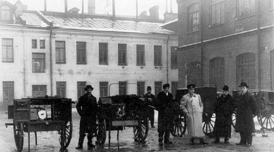    Военный министр В. А. Сухомлинов и сопровождающие его лица осматривают готовую продукцию - 4 типа кавалерийских радиостанций (слева направо) директор С. М. Айзенштейн, П. И. Балинский, В. А. Сухомлинов и А. В. Сисмон Фото: общественное достояние