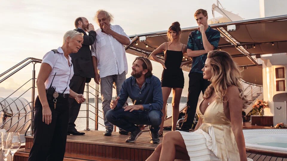 Для начала обратим внимание на очевидное высмеивание транснациональных корпораций. Репортёр модного журнала берёт интервью у молодых парней моделей, проходящих пробы в новое агентство и попутно шутя, представляя как бы выглядели фотосеты для разных брендов одежды. Одни и те же модели корчат различные гримасы, то серьёзные, то весёлые. Смысл данной можно описать как «каждому своё». Нравится покупателю серьёзная «Балленсиага» мы сделаем статусный вид, но сразу же при надобности поменяемся на семейную жизнерадостность у HandM. Очевидное подсвечивание лицемерия компаний ради собственной выгоды.