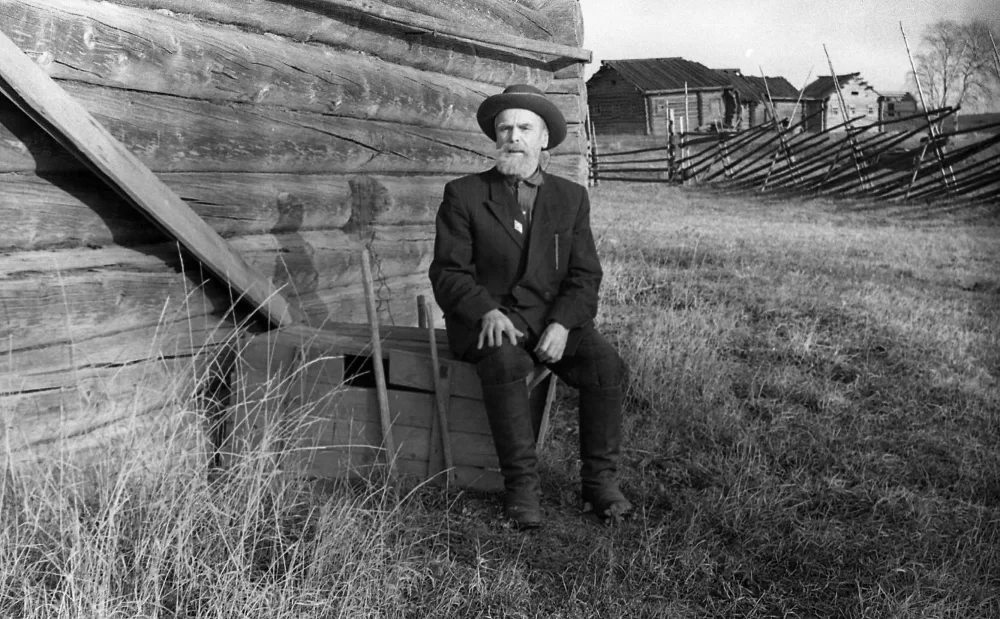  Житель деревни Омшев Федор Иванович сидит у своего дома