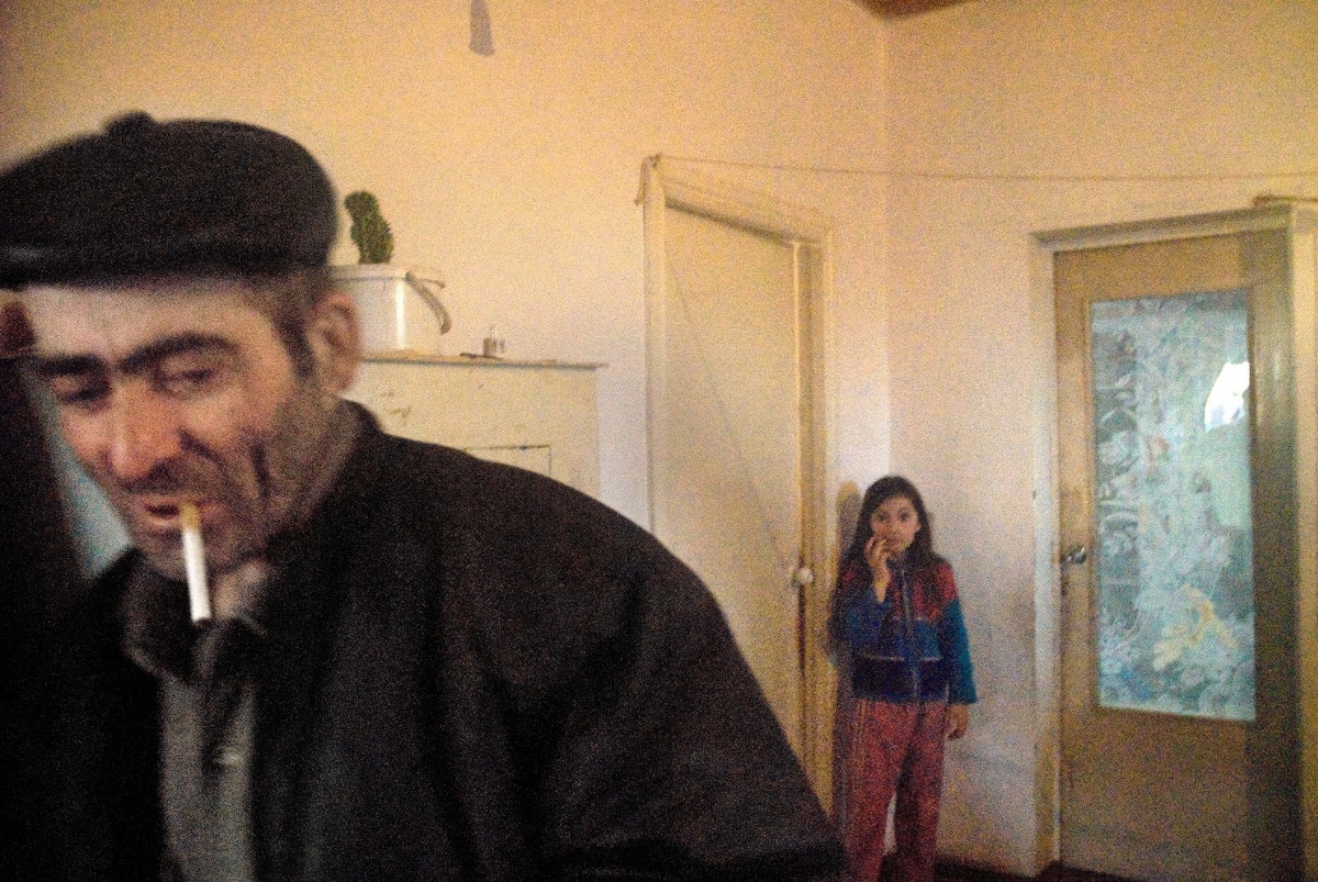 Нерезкое изображение мужчины с сигаретой, на фоне девочки у двери. Это идеально иллюстрирует грубую стилистику и непосредственность момента.