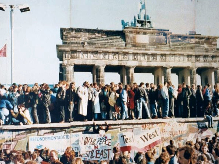     Берлинская стена с взобравшимися на нее немцами на фоне Бранденбургских ворот. / ru.wikipedia.org