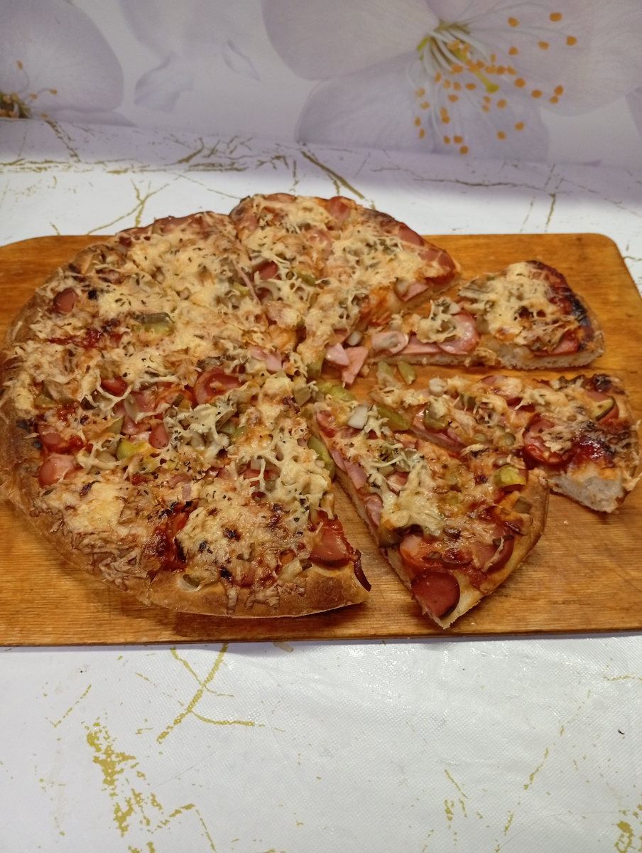 Пицца с сосисками, грибами и солеными огурцами под сыром.