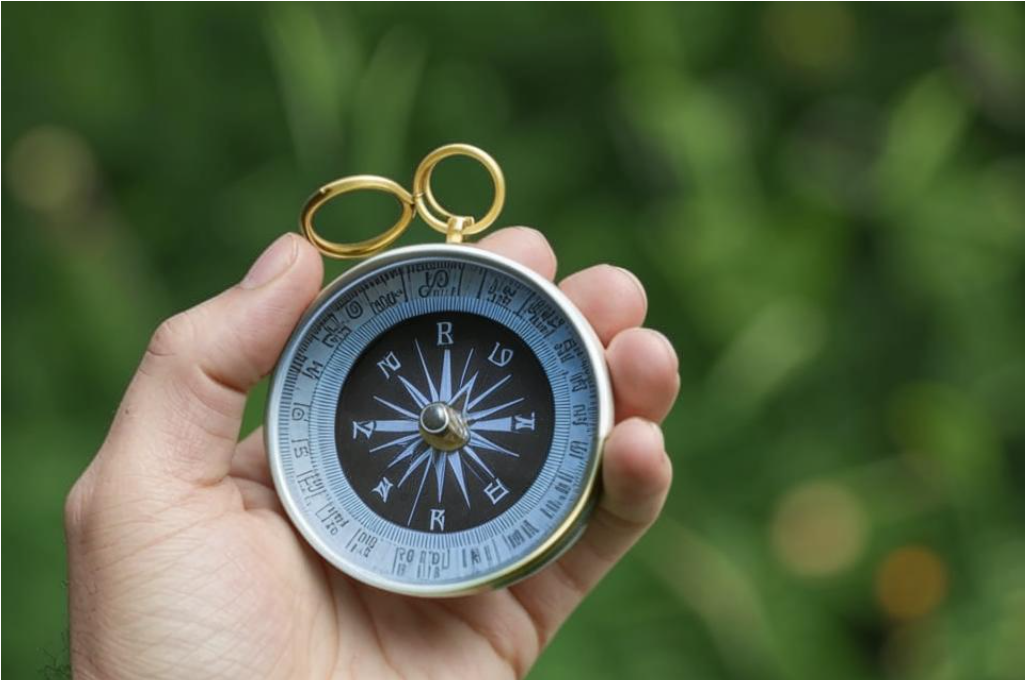 Рука человека, держащая компас, на фоне природы, как символ внутреннего ориентира.