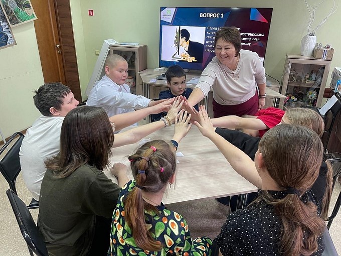 Подростки тянут руки друг к другу в центр стола