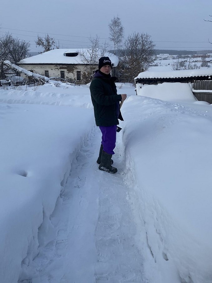 Молодой человек с лопатой чистит дорожку от снега