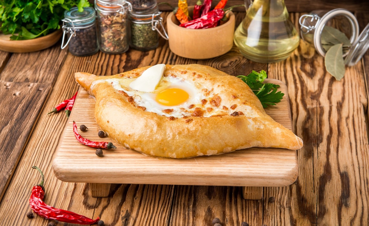 Хачапури – это традиционное грузинское блюдо, представляющее собой лепешку с сыром. Существует несколько видов хачапури, но самый популярный – хачапури по-аджарски, который имеет форму лодочки и сверху заливается яйцом. Однако классический вариант – просто круглая лепешка с сыром внутри. Вот рецепт простого хачапури:

### Ингредиенты для теста:
- Мука – 500 г
- Молоко теплое – 250 мл
- Дрожжи сухие – 7 г (или свежие дрожжи – около 20 г)
- Сахар – 1 ч.л.
- Соль – 0,5 ч.л.
- Масло растительное – 50 мл

### Для начинки:
- Сыр сулугуни или имеретинский сыр – 400 г
- Яйцо – 1 шт. (по желанию)
- Сливочное масло – 30 г (для смазывания готового хачапури)

### Приготовление:

#### 1. Подготовка теста:
1. В теплом молоке растворить сахар и дрожжи. Оставить на 10 минут до появления пены.
2. Добавить соль и растительное масло к молочной смеси.
3. Постепенно добавлять муку, замешивая тесто. Оно должно получиться мягким и эластичным.
4. Накрыть тесто полотенцем и оставить подходить в тепле на 1 час.

#### 2. Подготовка начинки:
1. Натереть сыр на крупной терке.
2. Если используется яйцо, добавить его к сыру и перемешать.

#### 3. Формирование хачапури:
1. Разделить подошедшее тесто на несколько частей (обычно получается 4-6 хачапури).
2. Каждую часть раскатать в круглую лепешку толщиной примерно 0,5 см.
3. На середину каждой лепешки выложить сырную начинку.
4. Края лепешки аккуратно собрать вверх и защипнуть, чтобы получился мешочек с сыром внутри.
5. Переверните мешочек швом вниз и снова слегка раскатайте, чтобы получилась плоская лепешка.

#### 4. Выпекание:
1. Разогреть духовку до 200°C.
2. Противень застелить пергаментом или смазать маслом.
3. Выложить хачапури на противень и выпекать 15-20 минут до золотистой корочки.
4. Готовые хачапури достать из духовки и сразу же смазать сливочным маслом.

Подавать горячими! Приятного аппетита!