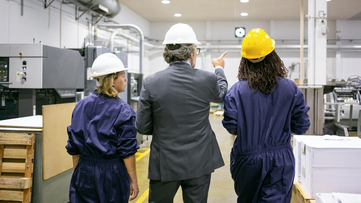 * - Руководитель и работницы фабрики в касках ходят по цеху и разговаривают