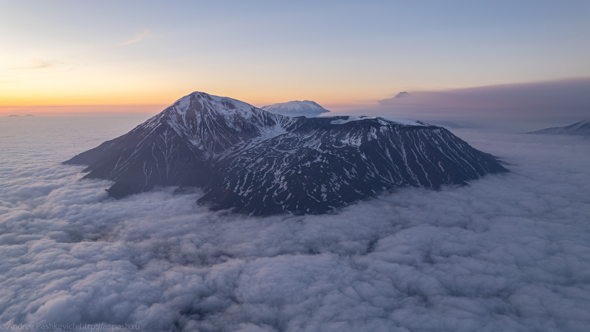 Вулканы Толбачик Острый и Плоский. За ним виднеется вулкан Ушковского (Дальняя Плоская), а правее на горизонте — Ключевская сопка в облаках.
