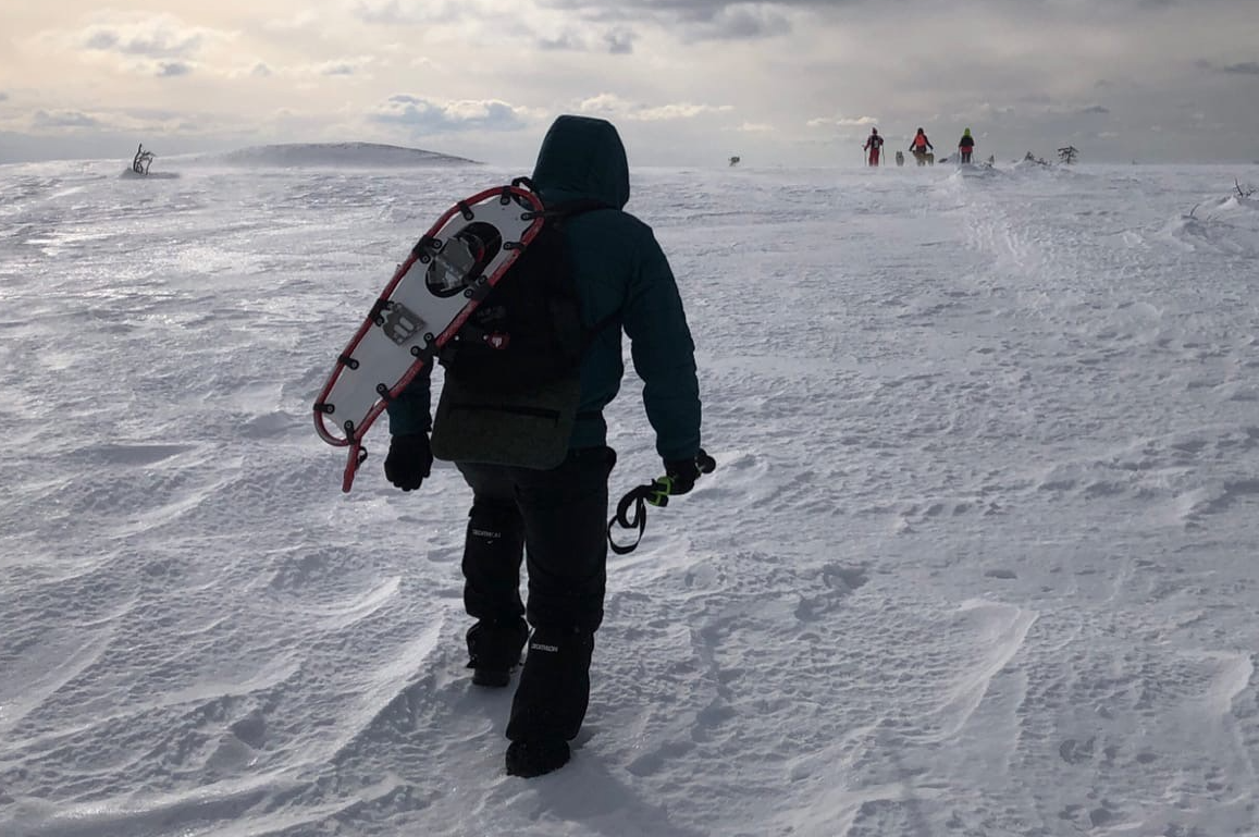 Турист движется по плотному снегу, закрепив снегоступы на рюкзаке