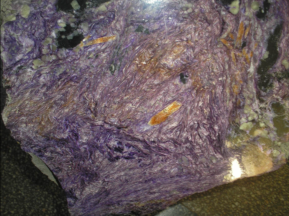 Отполированный чароитовый штуф в музее геологии Сибирского отделения РАН. Чароитом этот минерал назван по реке Чара - притоку реки Олёкма, впадающей в свою очередь в самую большую реку России Лену. Конечно же к этому названию присоединяется символическая этимология, связанная со словом "чарующий". "Запасы чароита оцениваются в несколько десятков тысяч тонн, при этом качество камня сильно варьируется от образца к образцу. Таким образом, на данный момент чароит остаётся самым редким и самым экзотическим драгоценным камнем на Земле, и найти аналогичное месторождение по-прежнему маловероятно даже в мировом масштабе.(В.А.Соляник, РАН, Владивосток, журнал Геммологической ассоциации Гонконга) 