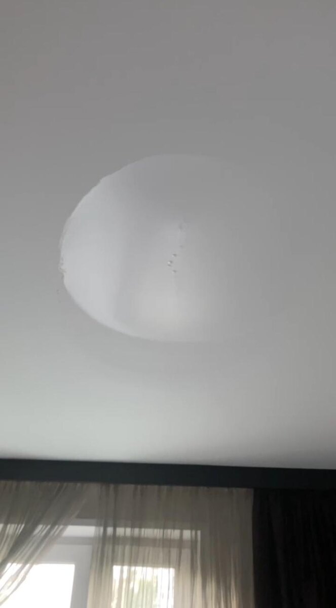 Мокрое пятно на тканевом потолке. В последствии станет жёлтым. Так же видны капли воды проступившие через полотно.