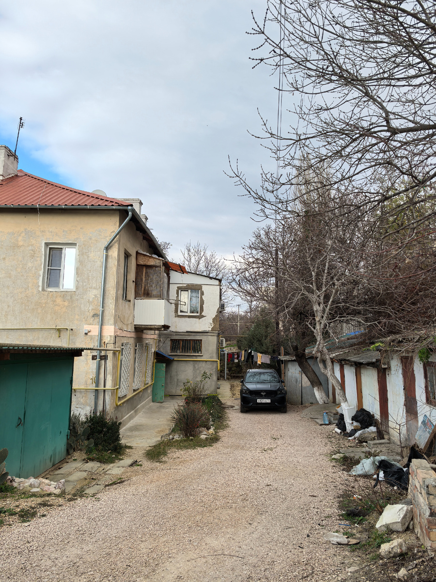 Там ещё бельё на верёвке сушится. И очень контрастно смотрится автомобиль на фоне старого дома и сарайчиков.