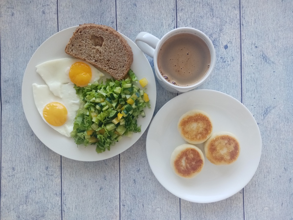 Завтрак. Яичница, салат, хлеб, сырники и кофе с молоком.