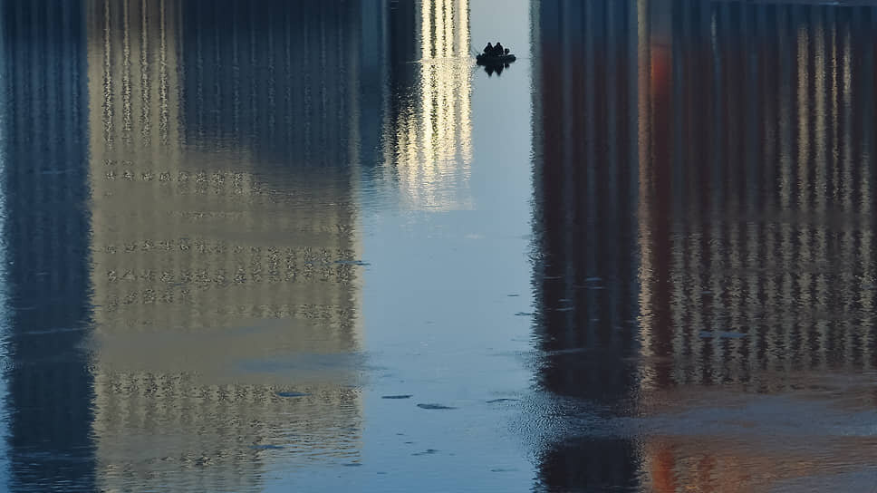 Отражение многоэтажных домов в воде и рыбаки на лодке на реке Обь в Новосибирске.📷Фото: Влад Некрасов / Коммерсантъ