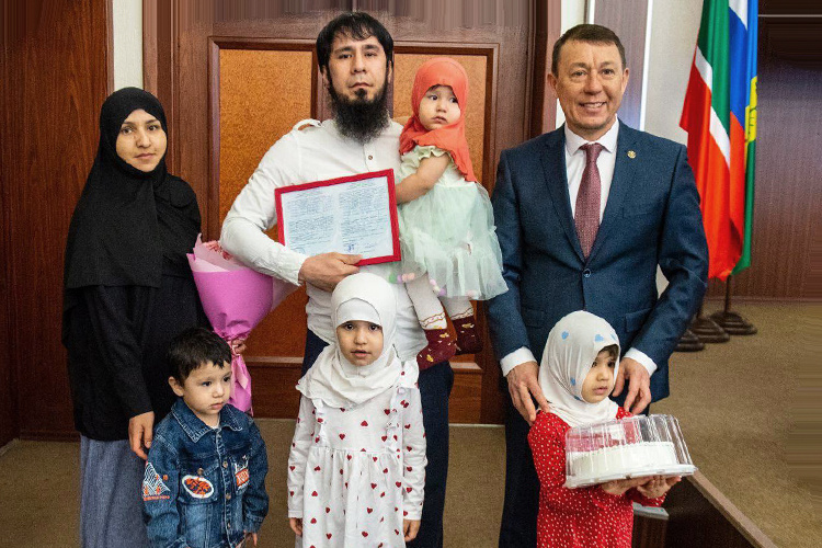    У Мухиддина Холзодова и Малики Тоировой четверо детей. Супруги — граждане РФ. Глава Нижнекамска Рамиль Муллин вручил им от государства сертификат на покупку жилья. Это вроде бы радостное событие вызвало негодование в соцсетях и проверку со стороны СК РФ.   
Фото: t.me/ramilmullin