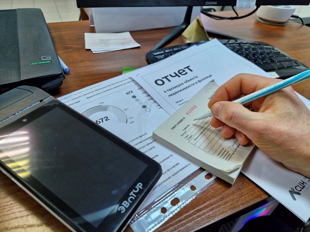 На изображении представлено оформление квитанции за предоставленные услуги агентства недвижимости, рядом с ней – отчет по проверке объекта и кассовый аппарат, подтверждающий точность финансовых расчетов.