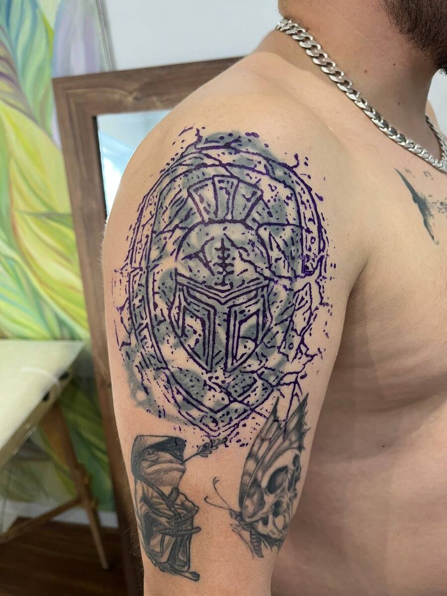 Вторая фотография демонстрирует нанесённый трансфер нового рисунка – спартанского шлема с щитом. Этот дизайн более детализирован и агрессивен, с чёткими линиями и элементами брони.