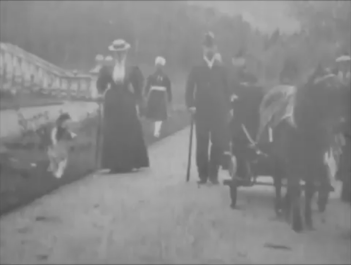 Кадр из хроники. Слева - императрица Александра Федоровна с собакой, за ней - Абдул Карим. Справа - коляска королевы Виктории, которую сопровождает император Николай II