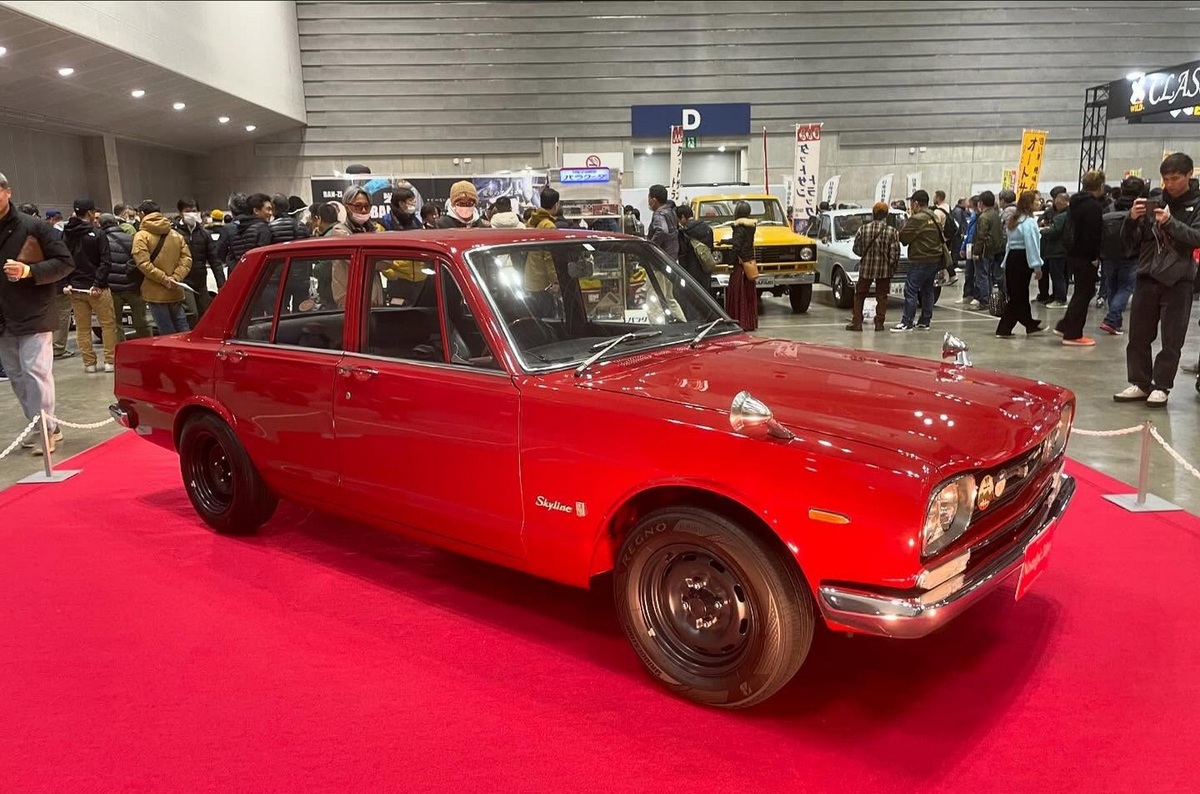    Мы как-то привыкли к тому, что Nissan Skyline GT-R — это двухдверное купе. Между тем, самый первый GT-R под заводским обозначением PGC10 выпускался с 1969 года именно в виде четырёхдверного седана, а купе освоили в производстве лишь осенью 1970-го. Перед нами — очень ранний седан 1969 года выпуска: буквально одна из пятидесяти первых машин. Этот автомобиль кирпично-бордового цвета украшал постер выставки. Напомним, что шестицилиндровые Скайлайны имели прогрессивное шасси с полностью независимой подвеской — на стойках Макферсон спереди и косых рычагах сзади. А версия GT-R получила почти гоночный мотор — шестицилиндровый S20 объёмом 2 литра, с четырёхклапанной головкой и тремя горизонтальными карбюраторами Mikuni-Solex, развивавший 160 л.с. В общей слощности было изготовлено 1945 машин этого поколения.   
The Deuce Factory