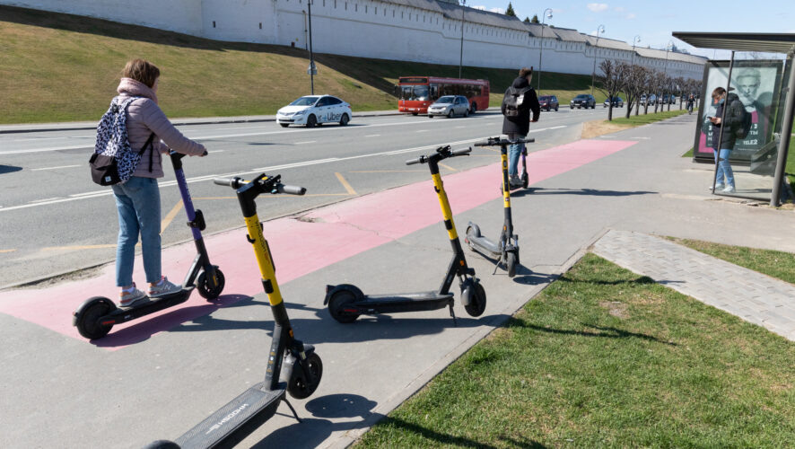    Молодые люди проезжают на электросамокатах мимо брошенных электросамокатов.