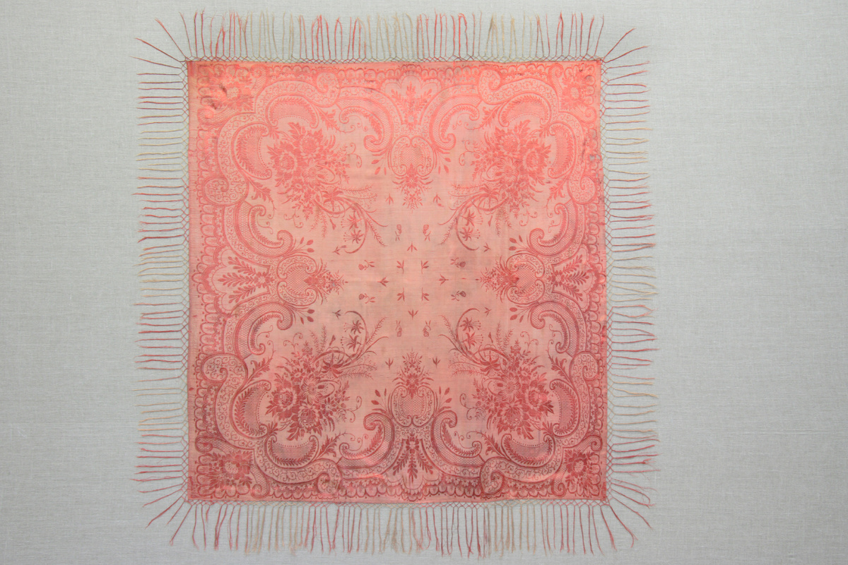 АМДЗ КП-14680. Т-2768 ШАЛЬ. Конец ХIХ - начало ХХ в. Ткань шелковая, фабричное производство. 132х125. На атласном фоне, вытканном из красных и серых нитей, - тканый красно-коричневыми шелковыми нитями узор. В среднике - небольшие веточки с бутонами и трилистники. В широкой кайме - вазоны, ветки и травы; в углах - крупные букеты из цветов и трав. По краям - кисти из серых и красно-коричневых шелковых нитей. Экспедиция в Мезенский район, 2000.