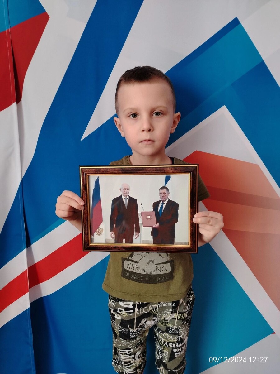 Внук Николая Гордей держит фото, на котором Р. Хамитов вручает его деду благодарственное письмо.