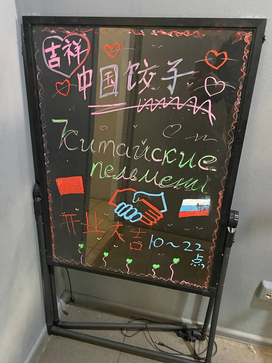 Вывеска на входе с использованием двух языков. Сверху на китайском написано "китайские пельмени", а снизу - пожелание успехов (китайская традиция)