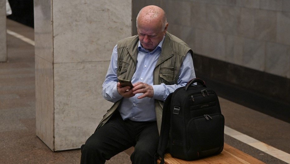   Пенсионер просматривает сообщения в телефоне, ожидая поезд на станции метро. Автор фото: Михаил Тихонов / "Деловой Петербург"