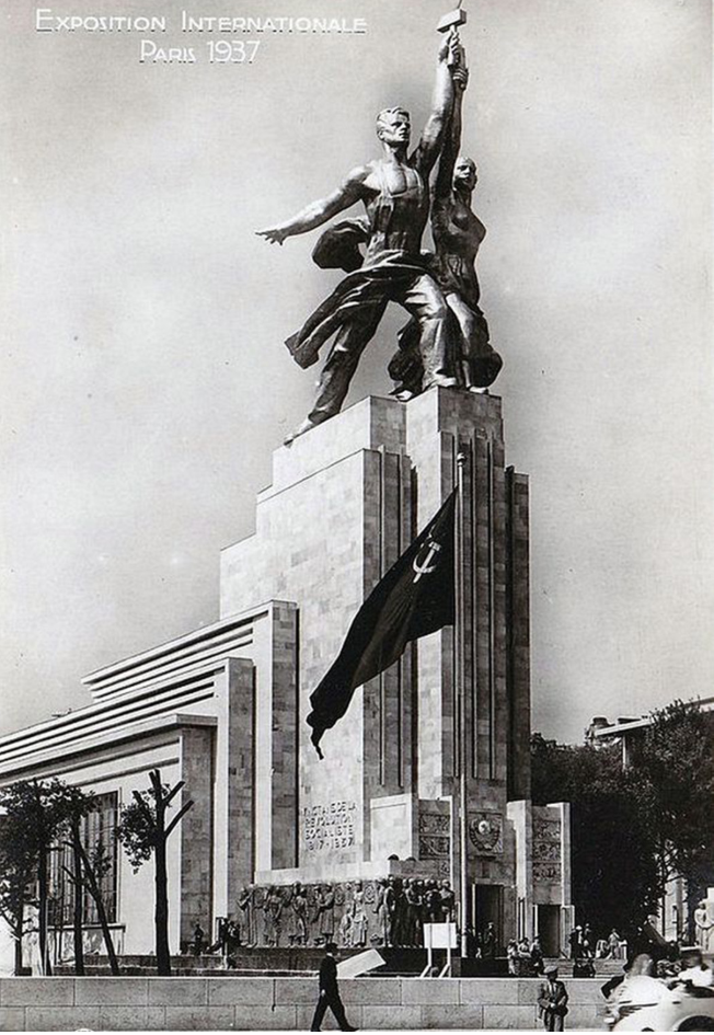 Павильон СССР на Всемирной выставке 1937. Наверху — скульптура "Рабочий и колхозница" В.И. Мухиной. Над входом — герб СССР и барельефы "Народы СССР" работы В.А. Фаворского. Сбоку павильона — надпись "20 лет социалистической Революции". Перед павильоном — пропилеи с барельефами на тему народов СССР работы И.М. Чайкова. 