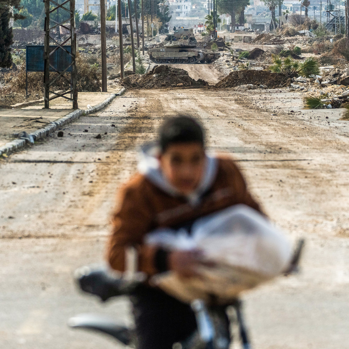 Мальчик несёт домой буханку хлеба, пока израильские военные машины блокируют дорогу, ведущую в сирийский город Кунейтра, 5 января 2025 года. Мосааб Эльшами | AP.