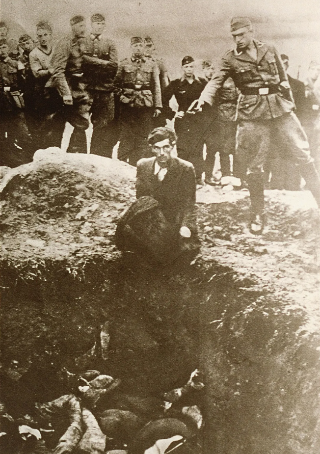 Айнзацгруппы. Член айнзацгруппы, специального мобильного подразделения СС, готовится застрелить украинского еврея, стоящего на коленях на краю братской могилы.