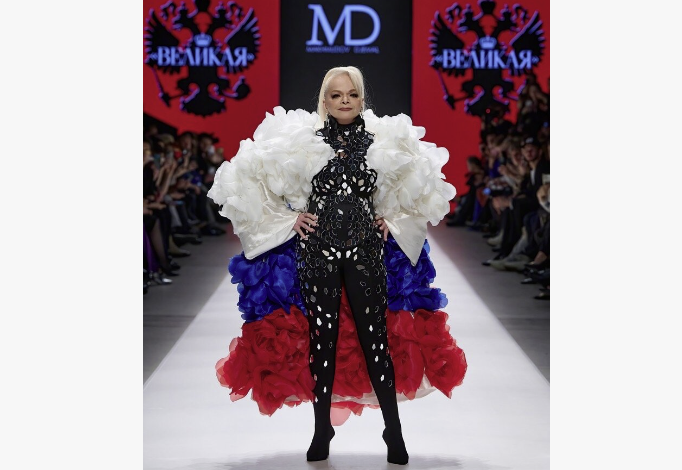 Кадр из модного показа, где у артистки костюм с накидкой в трех цветах…