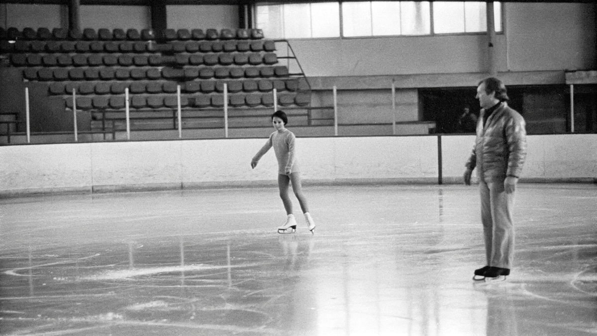 На фото: Юная фигуристка во время индивидуальной тренировки в полупустом зале с тренером, начало 1970-х