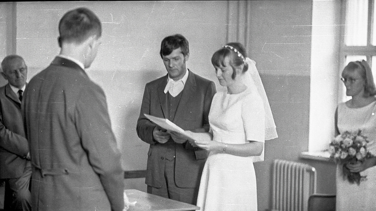 Молодожены в скромных нарядах подписывают документы в присутствии работника ЗАГСа и свидетелей