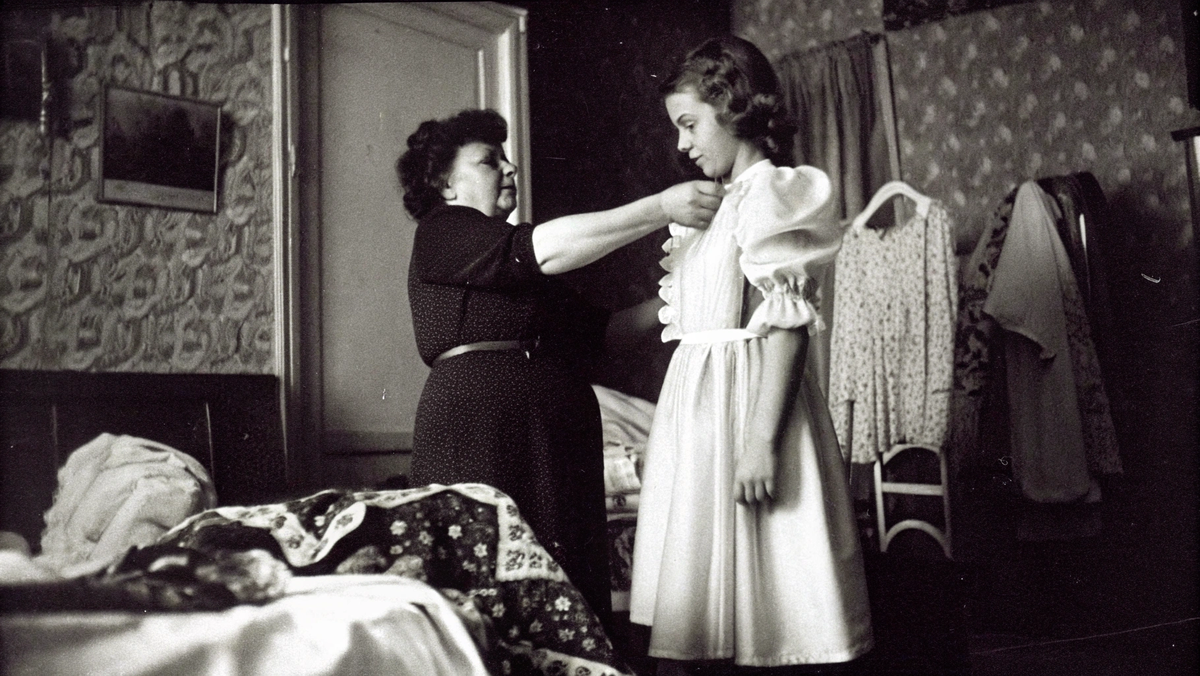 Бабушка помогает дочери примерить белое платье, готовясь к школьным танцам