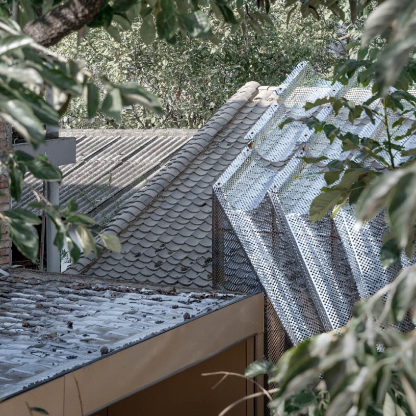 Волнообразная перфорированная металлическая крыша, которая напоминает плавную черепицу на крышах местных домов.