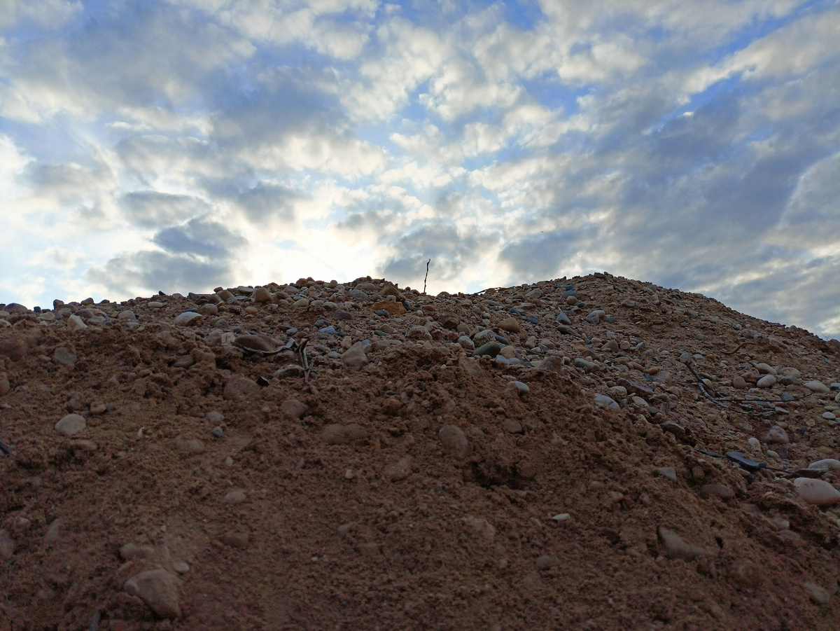 Куча песка с камнями. За нею – солнце в облаках, стремящееся к западу (фото автора)
