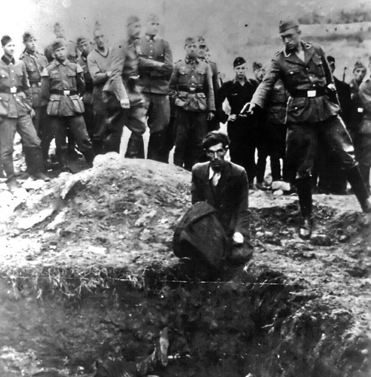 Айнзацгруппы. Член айнзацгруппы, специального мобильного подразделения СС, готовится застрелить украинского еврея, стоящего на коленях на краю братской могилы.