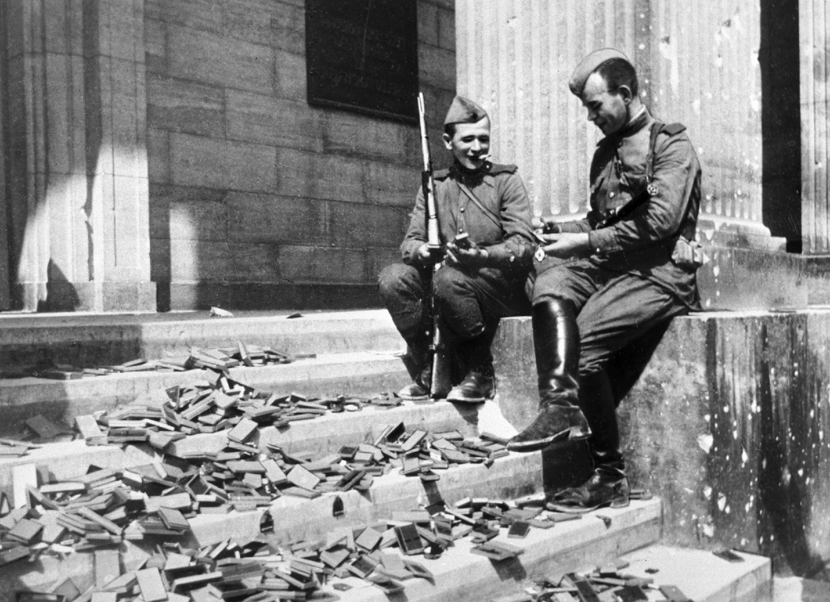 Воины-победители сидят на ступеньках Имперской канцелярии в Берлине, рассматривая железные кресты, запасы которых были не использованы для награждения немецких солдат. 15.05.1945 г. Фото Евгения Халдея