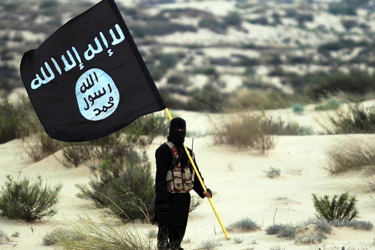 Член «Исламского государства Ирака и Леванта» (ИГИЛ). Боец в маске позирует в пустыне в Ираке или Сирии, держа в руках флаг «Исламского государства Ирака и Леванта» (ИГИЛ). 