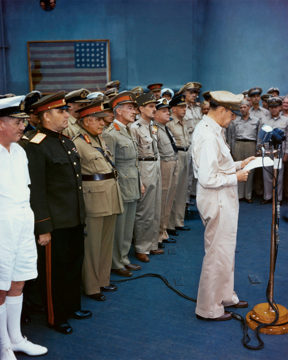 Капитуляция Японии, сентябрь 1945 года. Генерал Дуглас Макартур читает документ во время церемонии капитуляции на борту линкора «Миссури» (BB-63) в Токийском заливе, 2 сентября 1945 года. Представители стран-союзниц стоят за ним.. Источник изображения: сайт worldofwarships.com
