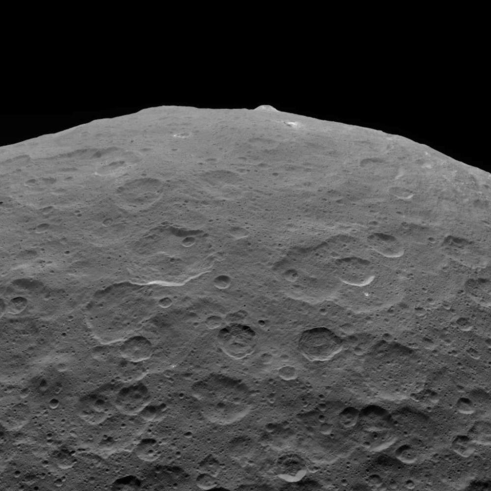 Эта фотография Цереры и одной из ее главных достопримечательностей, горы Ахуна, была одним из последних изображений, переданных зондом Dawn. Этот вид, обращенный на юг, был запечатлен 1 сентября 2018 года на высоте 2220 миль (3570 километров). Ahuna Mons имеет около 12 миль (20 километров) в поперечнике и 2,5 мили (4 километра) в высоту и демонстрирует карбонат натрия вдоль своих склонов.