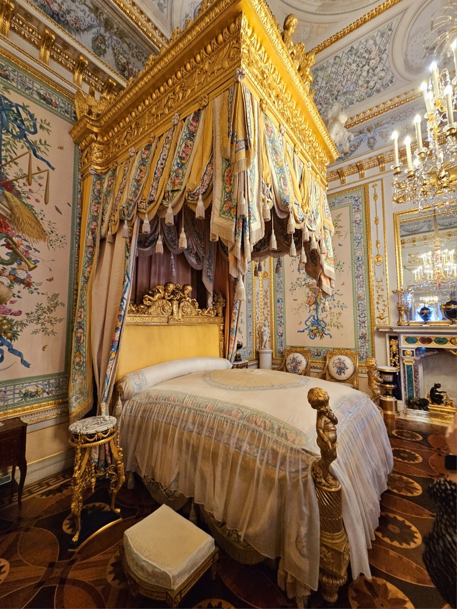 Парадная кровать помещена против окон под балдахином. Высокая спинка украшена декоративной резьбой с изображением ваз с цветами, жертвенника любви с парящими над ним амурами и целующимися голубками, здесь же сфинксы, символы вечности, и «недреманное око», и гончие собаки, символы верности. По борту спинки изображены знаки Зодиака.