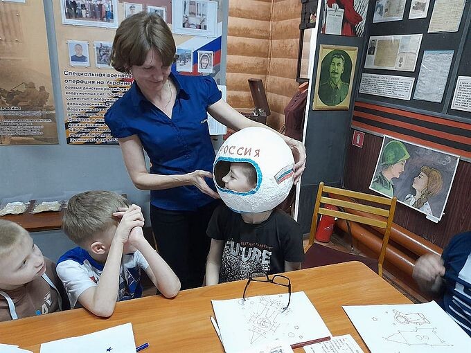 Сотрудник музея помогает мальчику примерить муляж скафандра