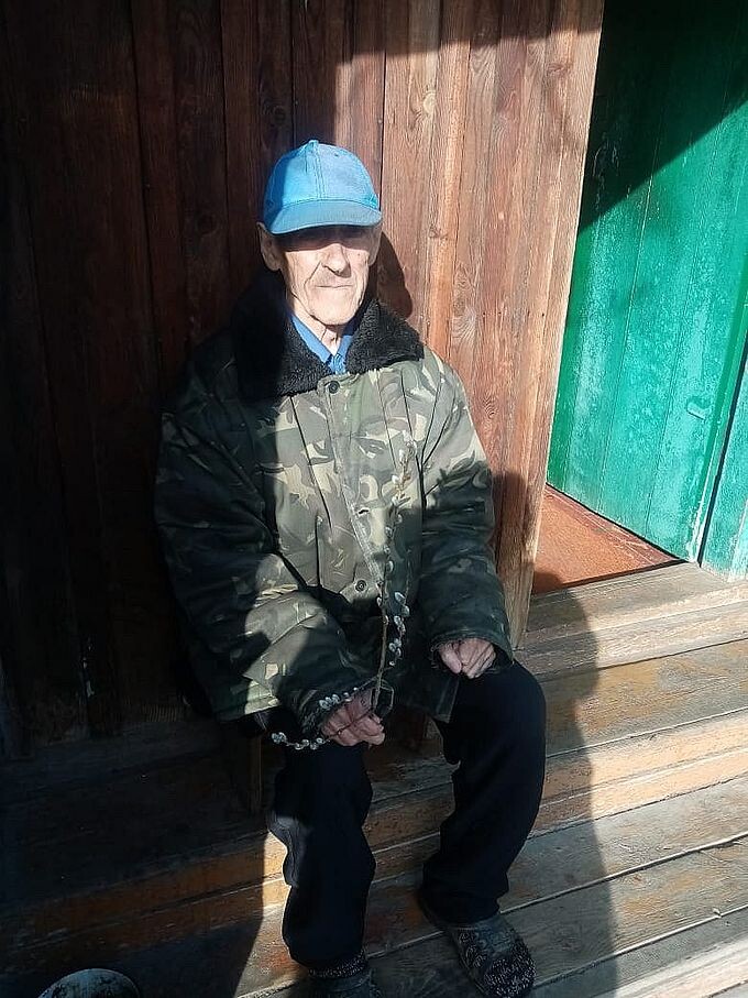 Пожилой мужчина сидит на крыльце, держа в руке подаренную ему веточку вербы