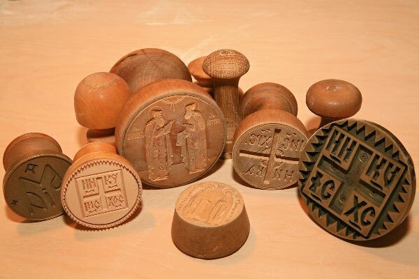 Раскладываем заготовки на отдельной доске (обязательно натерев мукой, чтобы не прилипали) и накрываем двумя полотенцами – сухим и влажным. Включаем духовку – верхний и нижний нагрев – на 210 градусов. Через 10 минут ставим печати на верхние части просфор, промазываем верхушки и донышки водой и накладываем верхушки на донышки горизонтально.
