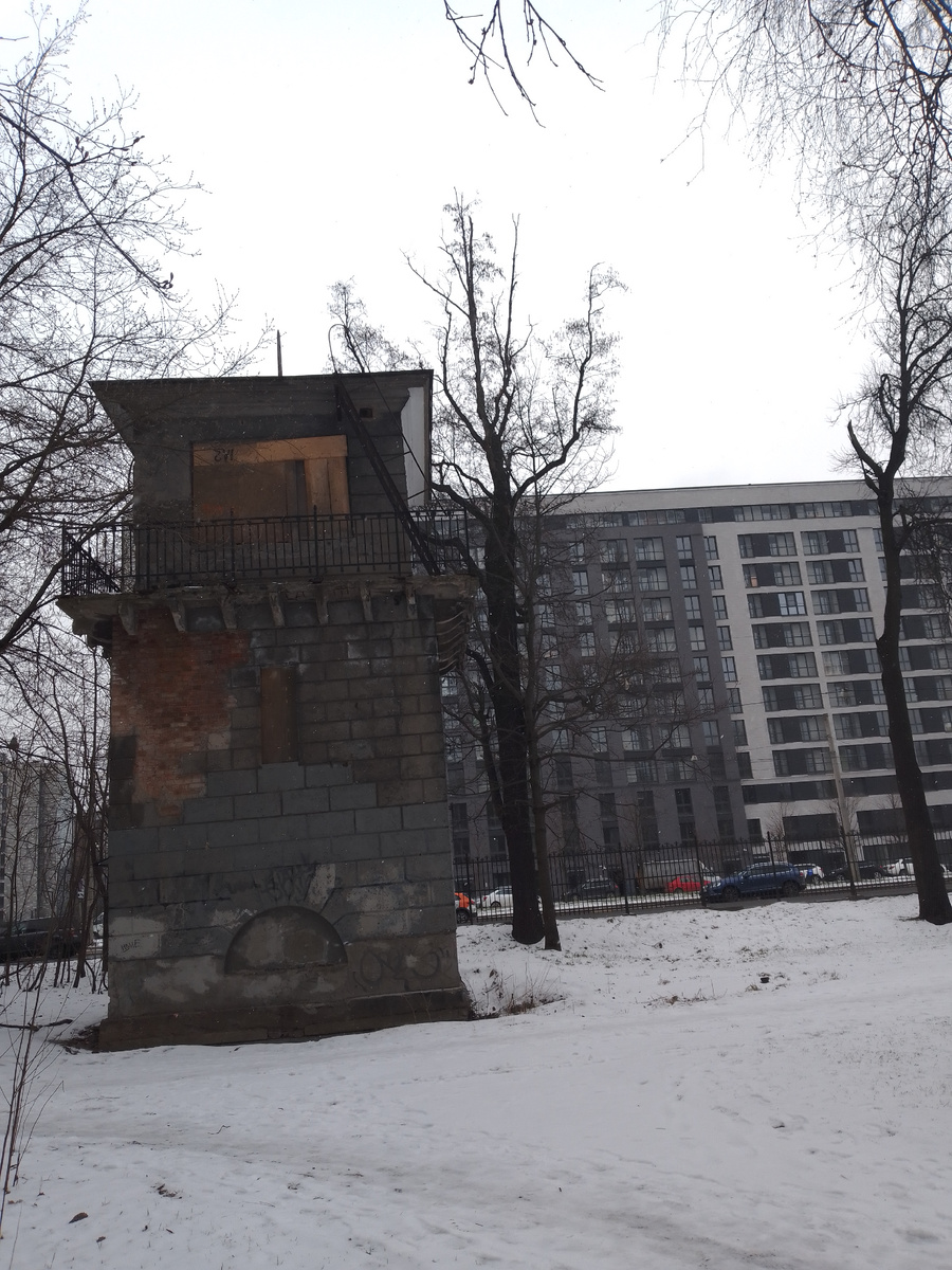 Даже на фоне современного дома башня неплохо смотрится. Уже облицовка отвалилась с западной стены. С южной стены уже нет решетки балкона, с которого дежурный наблюдал за поездом и перекрывал проспект Энегельса. 